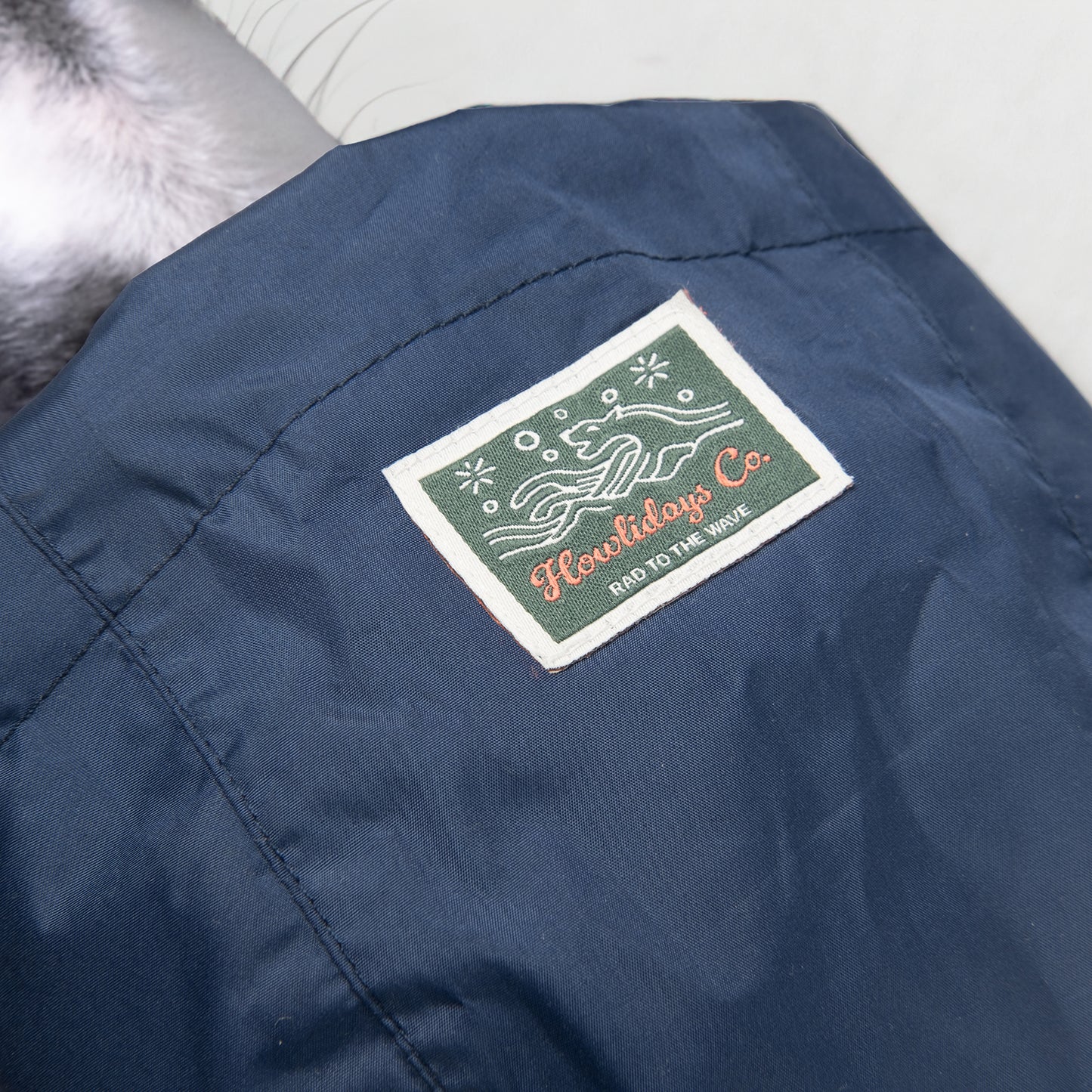 Close-up of the woven label on the Baja Coastline all-weather dog coat, featuring an ocean-inspired dog emblem with Howlidays Co. branding.